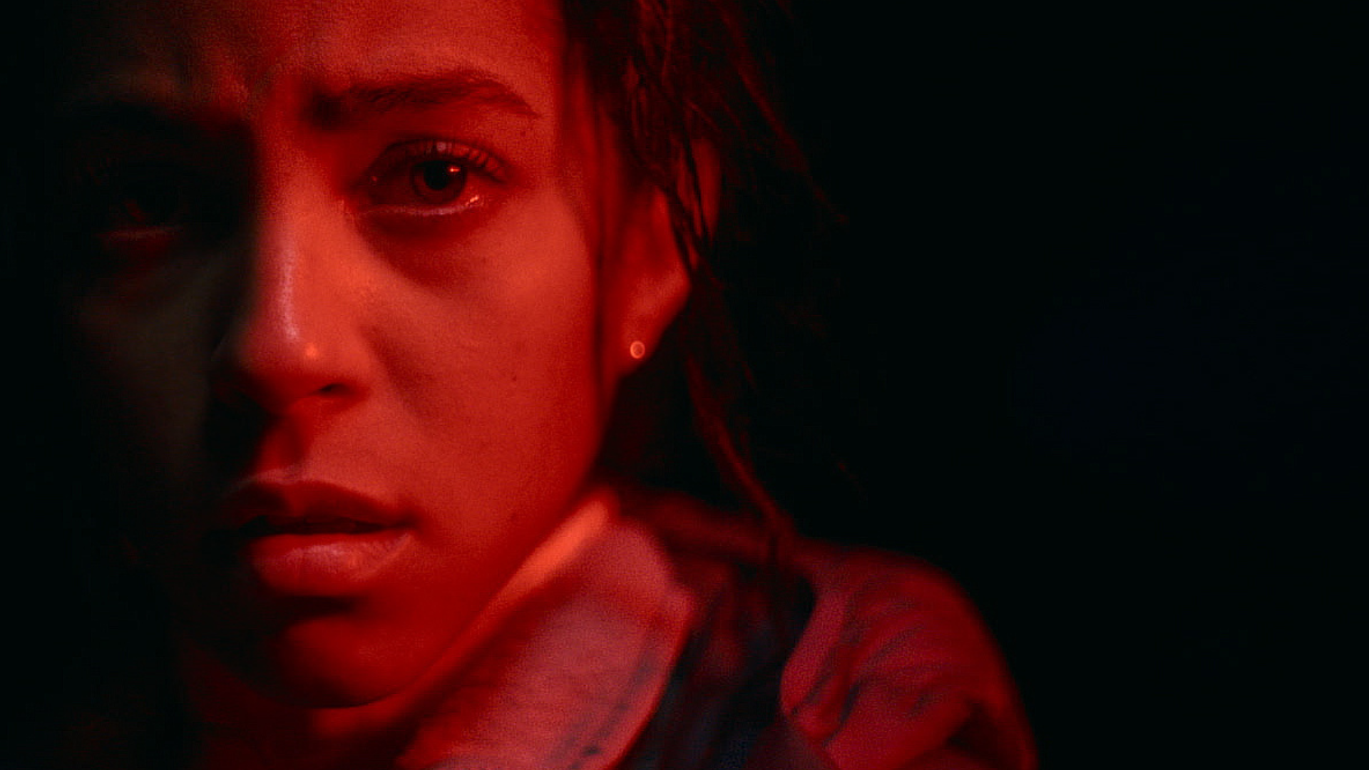 Close-up of a young person's face bathed in red light against a dark background.